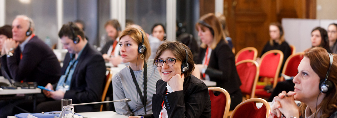 Participant in the EC conference 'Privacy' with interpreting headphones looks friendly into the camera and supports her head on her hand.